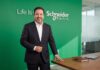 Schneider Electric: Crecer por etapas; por qué la infraestructura para IA empieza a diseñarse con mayor flexibilidad Fotografía en plano medio de José Alberto Llavot, Gerente de Preventa y Desarrollador de Negocios en Schneider Electric para México y Centroamérica, vistiendo saco oscuro sobre camisa blanca, posando sonriente y apoyado en una mesa de madera de sala de juntas frente a un muro verde con el logotipo corporativo iluminado.