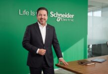 Schneider Electric: Crecer por etapas; por qué la infraestructura para IA empieza a diseñarse con mayor flexibilidad Fotografía en plano medio de José Alberto Llavot, Gerente de Preventa y Desarrollador de Negocios en Schneider Electric para México y Centroamérica, vistiendo saco oscuro sobre camisa blanca, posando sonriente y apoyado en una mesa de madera de sala de juntas frente a un muro verde con el logotipo corporativo iluminado.