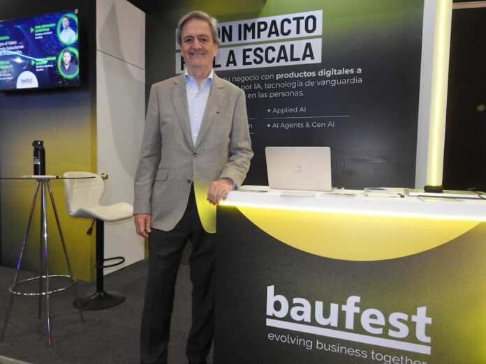 Luis Battilana expone el enfoque de negocio para escalar la inteligencia artificial en Baufest Fotografía en plano medio de Luis Battilana, Country Manager de Baufest, sonriendo en un saco claro sobre una camisa de vestir azul, apoyado en el mostrador iluminado del estand de Baufest bajo el lema