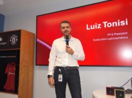 Orquestando el futuro digital: El poder de la IA Agéntica de Snapdragon Fotografía en plano medio de Luiz Tonisi, VP y Presidente de Qualcomm Latinoamérica, vistiendo camisa blanca de botones y pantalón negro, hablando al micrófono frente a una pantalla roja corporativa que muestra su nombre y cargo.