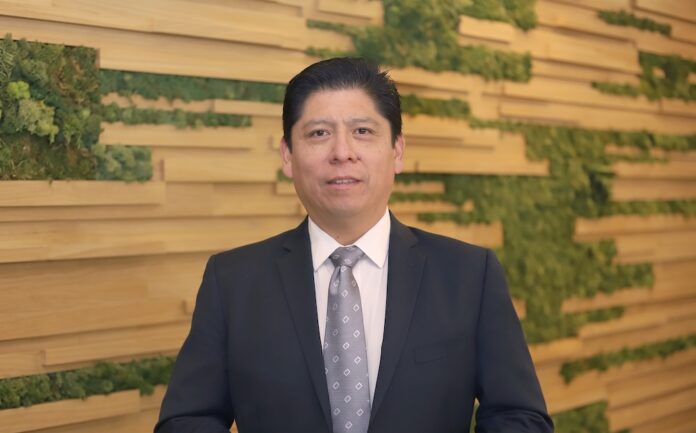 Fotografía de retrato corporativo en plano medio de Martín Hoz, Vicepresidente Sénior de Ingeniería de Preventa de Fortinet para América Latina y el Caribe, vistiendo traje oscuro con corbata gris estampada y sonriendo frente a un muro decorativo de paneles de madera y follaje verde.