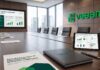 Veeam lanza un programa global para garantizar el control y la soberanía de los datos Fotografía de una sala de juntas ejecutiva de Veeam Software con ventanales hacia la ciudad, que muestra en la pared una pantalla con la presentación "El Control de la Soberanía de sus Datos", sobre la mesa una tableta digital con métricas de gobernanza y un documento impreso sobre el Programa Global de Proveedores de Servicios Soberanos.