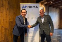 Tasmicro incorpora Noma Security a su portafolio para fortalecer la seguridad y gobernanza de agentes de IA en México y Latinoamérica Fotografía de plano medio de Víctor Anda, Director Regional de Ventas para Latinoamérica de Noma Security, estrechando la mano de Sergio Hernández, Socio Director de Tasmicro, sonriendo frente a un banner publicitario de Noma Security en una oficina con acabados de madera.