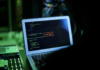 Norton revela que 83% de los mexicanos sufrió ciberamenazas en el último año pese al descuido en seguridad básica Fotografía en ángulo dorsal de un usuario frente a la pantalla de una computadora portátil en una habitación oscura con iluminación verde, donde se observan líneas de código de programación y una ventana de alerta roja central con el texto "Access Denied".
