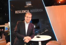 El escudo digital del futuro financiero y corporativo con GM Sectec Fotografía en plano medio de Octavio Osorio, Director General y Vicepresidente de Operaciones Internacionales de GM Sectec, apoyado en una mesa alta blanca en su estand corporativo bajo el lema "RESILIENCIA, INTEGRADA."