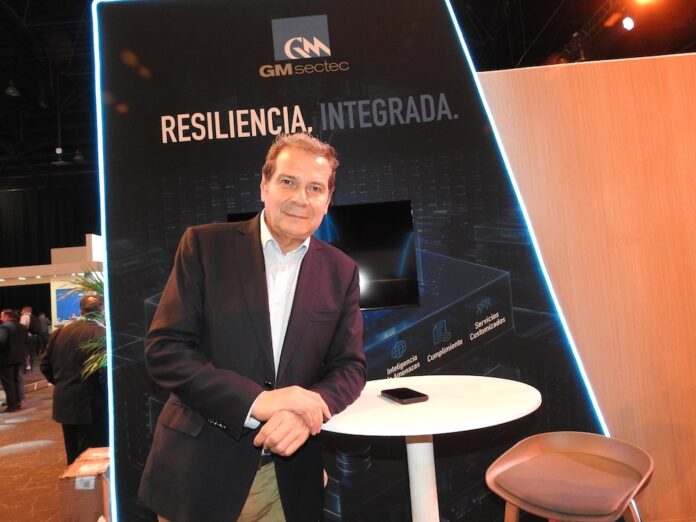 Fotografía en plano medio de Octavio Osorio, Director General y Vicepresidente de Operaciones Internacionales de GM Sectec, apoyado en una mesa alta blanca en su estand corporativo bajo el lema 
