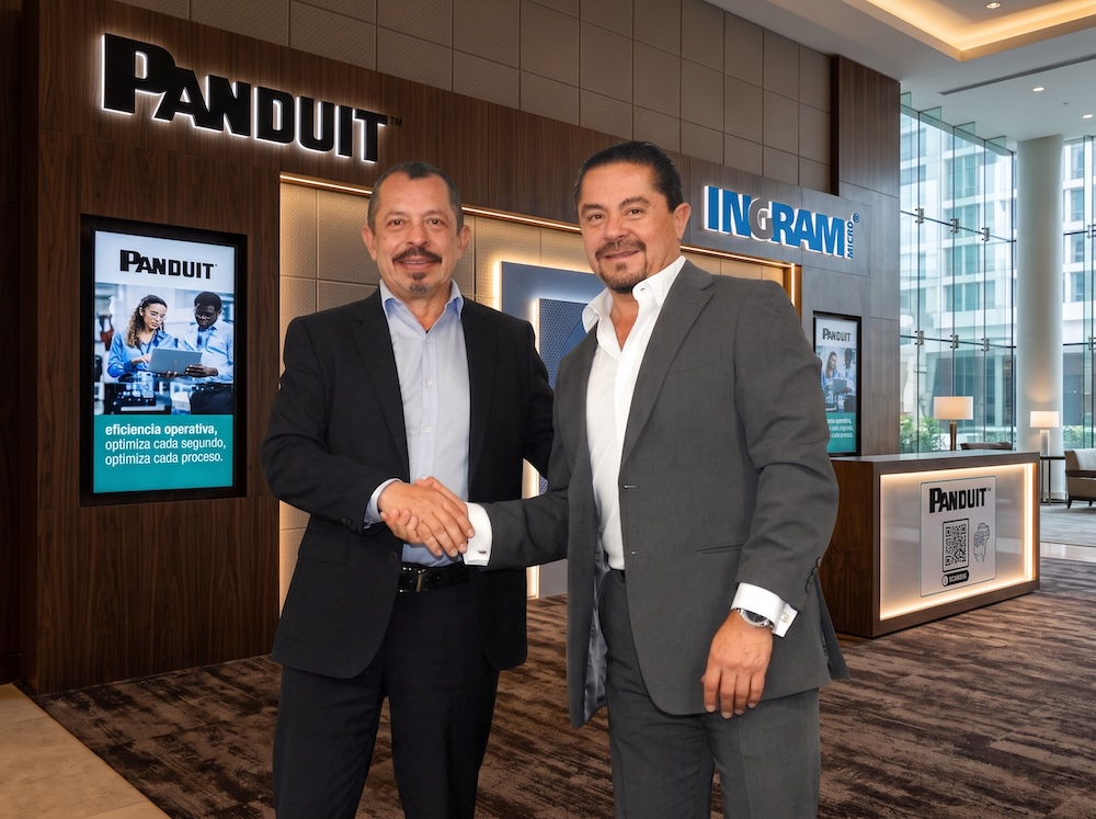 Panduit e Ingram Micro México formalizan alianza estratégica para la distribución de infraestructura física Fotografía en plano medio de Carlos Arochi, Director de Panduit Latam, y Gerardo Romero, Director de Ingram Micro México, estrechando la mano sonrientes frente a los logotipos iluminados de Panduit e Ingram Micro en un entorno corporativo.