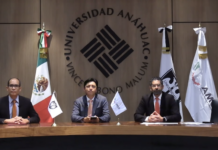Hacia una resiliencia digital inquebrantable en el 3er Foro Nacional de Ciberseguridad Fotografía en plano general de la mesa presidium con José Manuel Santiago, Ernesto Ibarra y Eugenio Valle sentados frente al gran escudo grabado en madera de la Universidad Anáhuac México, flanqueados por la bandera nacional y estandartes institucionales.