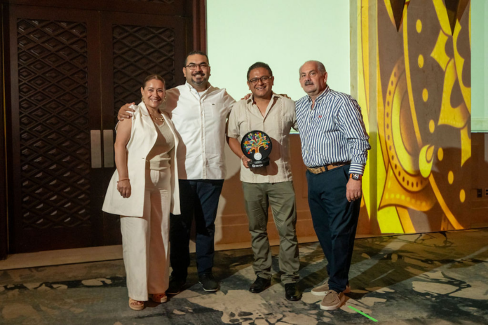 Reyes Hernández y el equipo directivo de CT Internacional exhiben el trofeo otorgado por Xerox Fotografía de grupo en plano medio de cuatro ejecutivos de CT Internacional y Xerox, donde el representante central viste una guayabera beige y sostiene con orgullo una estatuilla conmemorativa en forma de árbol multicolor sobre una base negra de Xerox.