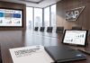 SAP presenta la Empresa Autónoma impulsada por Joule y SAP Business AI Platform Fotografía de una sala de juntas ejecutiva de SAP con un ventanal hacia un panorama urbano, que muestra en la pared una pantalla con la presentación "La Empresa Autónoma en Acción", sobre la mesa una tableta digital con paneles de rendimiento y un reporte impreso sobre el impacto de la IA en los negocios.