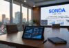 SONDA impulsa la transformación operativa como motor clave de la competitividad del retail mexicano Fotografía en perspectiva de una sala de juntas corporativa con vista a la ciudad al atardecer, mostrando sobre la mesa de madera una tableta digital con gráficas de procesos logísticos y comercio electrónico, y al fondo una pantalla interactiva con el logotipo de SONDA y la frase "La transformación operativa: clave para la competitividad del retail mexicano".