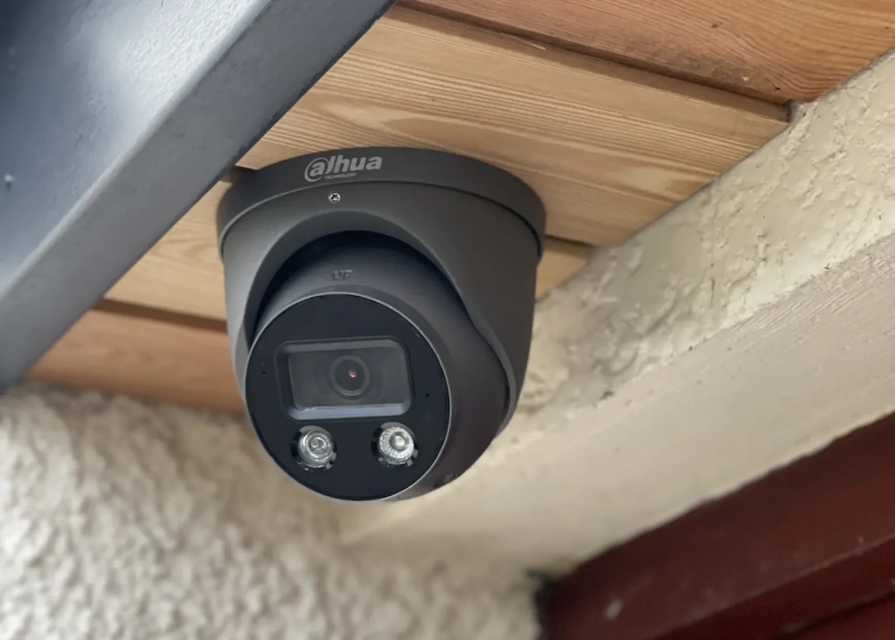 Fotografía en plano medio de una cámara de seguridad tipo domo exterior marca Dahua de color gris oscuro, instalada en el plafón de madera del techo de un inmueble.