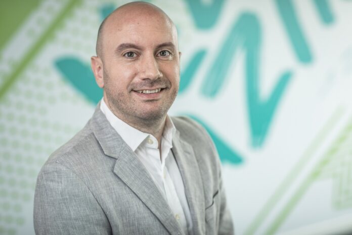 Tomas Dacoba impulsa la evolución hacia la resiliencia cibernética y la protección de datos en Veeam Fotografía de retrato corporativo en primer plano de Tomas Dacoba, sonriendo en saco gris claro sobre un fondo con patrones gráficos en tonos verde y blanco.